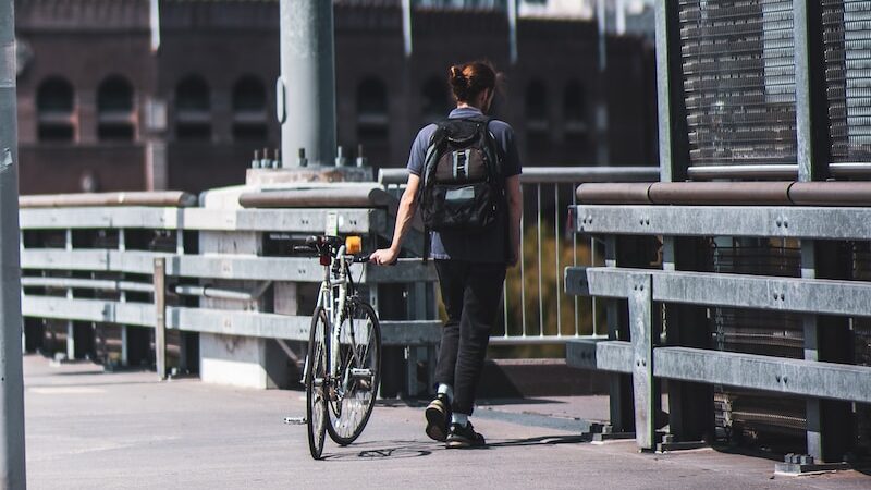 man in black jacket and blue denim jeans riding bicycle on road during daytime